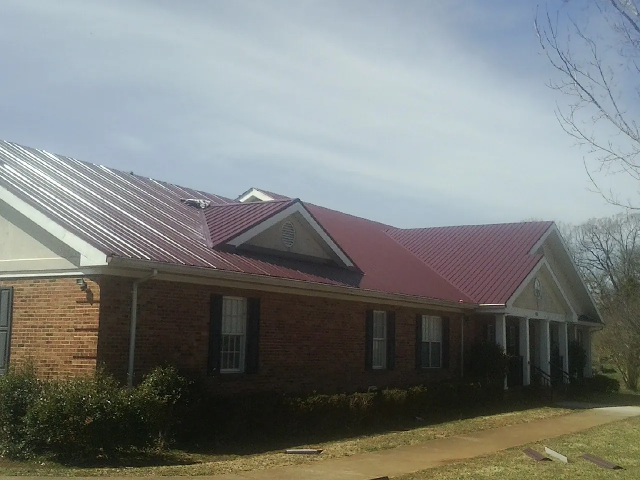 Red metal roof with gabled entries on a long brick building, from a Hail Damage Roof Repair job in Burton