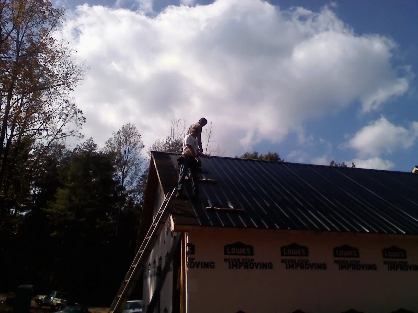 Roofer fastening dark metal panels high against a cloudy sky, from a Roof Inspection job in Burton