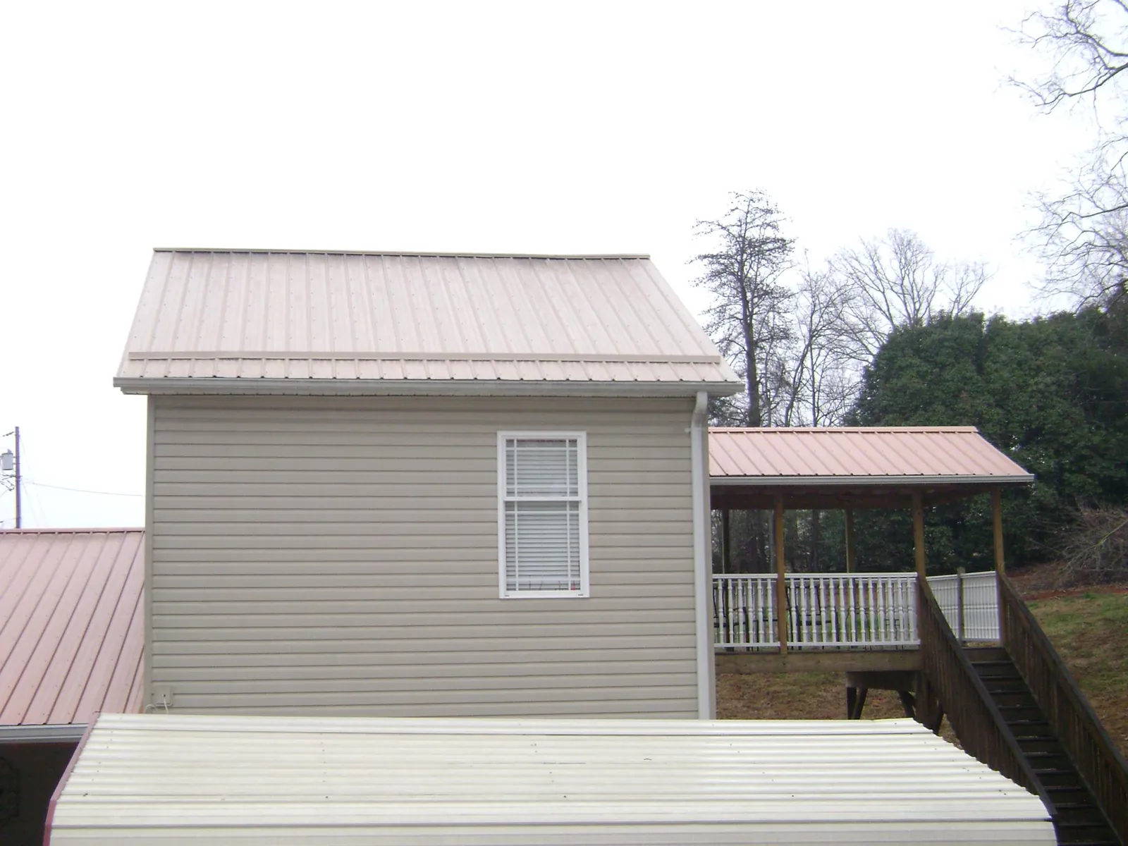Tan metal roofs on a two story addition and attached porch, from a Roof Replacement job in Burton
