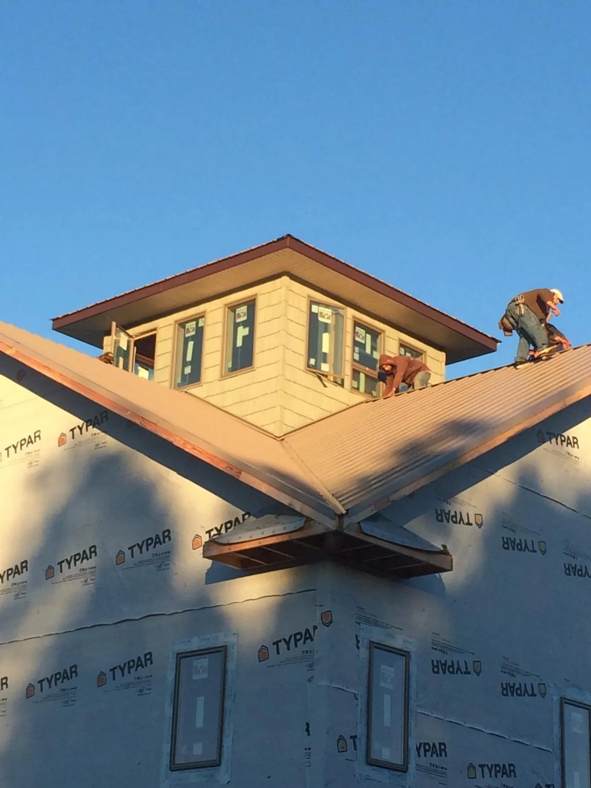 Roofers working around a rooftop cupola on a new metal roof at sunset — Roof Waterproofing in Burton by Roofing Brothers